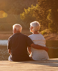 Elderly couple sitting together on a wooden dock by the water