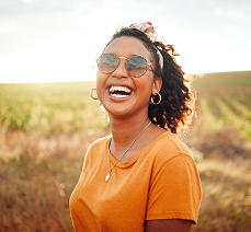 Woman laughing outdoors wearing sunglasses on a sunny day