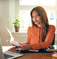 Black woman at her desk carefully reviewing financial documents
