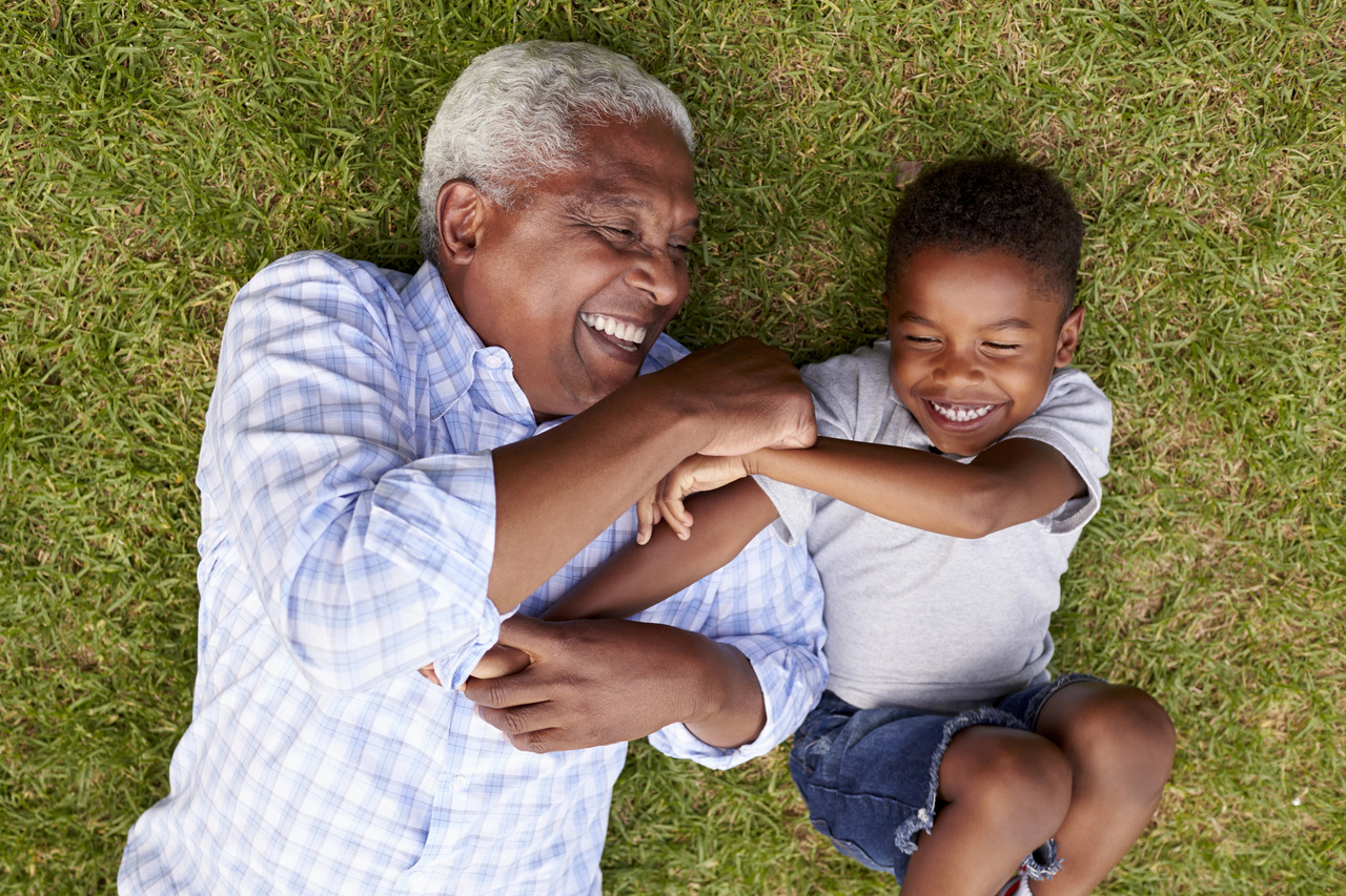 Grandfather and young grandson laughing together while lying on a grassy lawn