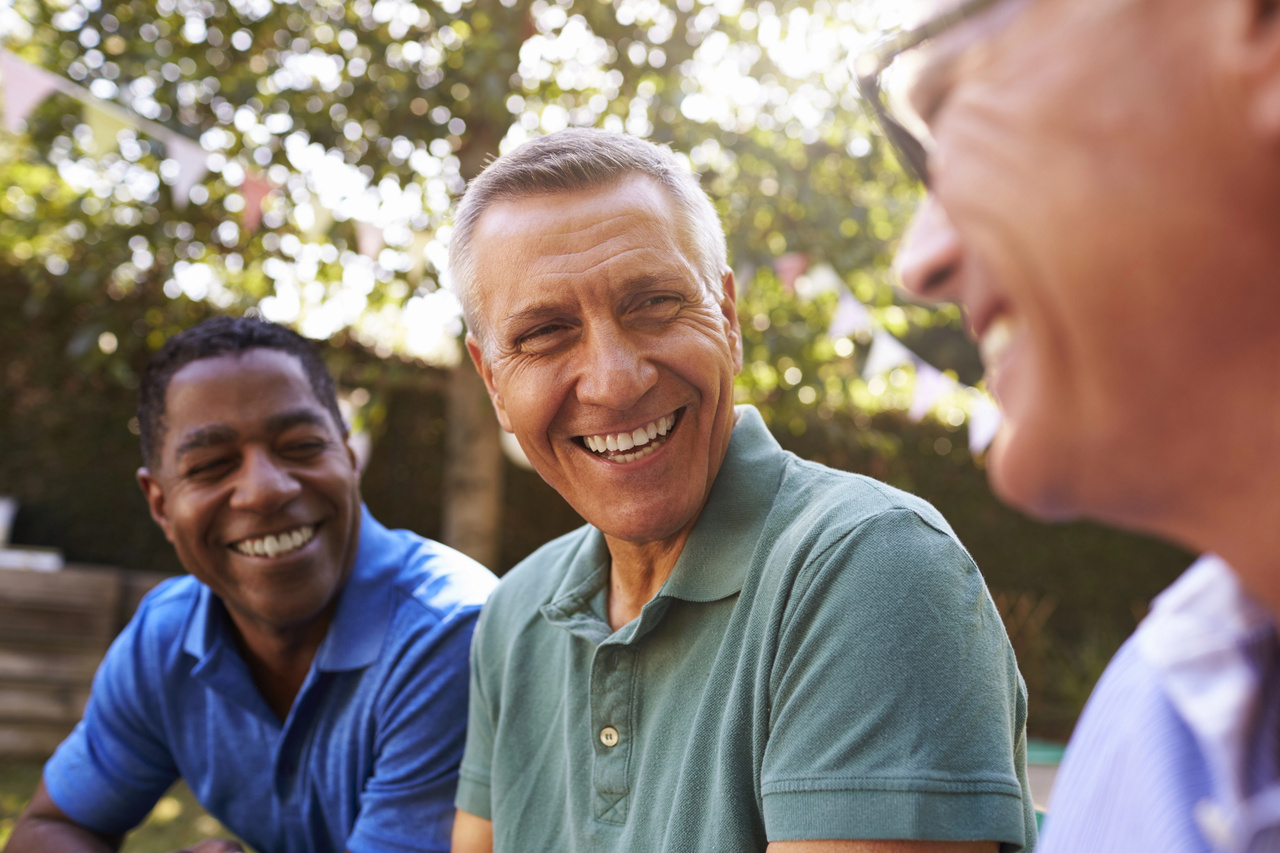 Three older men laughing and socializing together outdoors in a garden setting