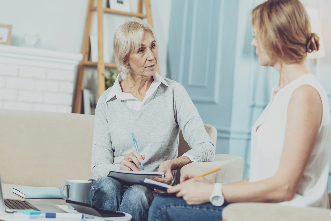 Senior woman and younger woman in a serious financial consultation, both taking notes at home