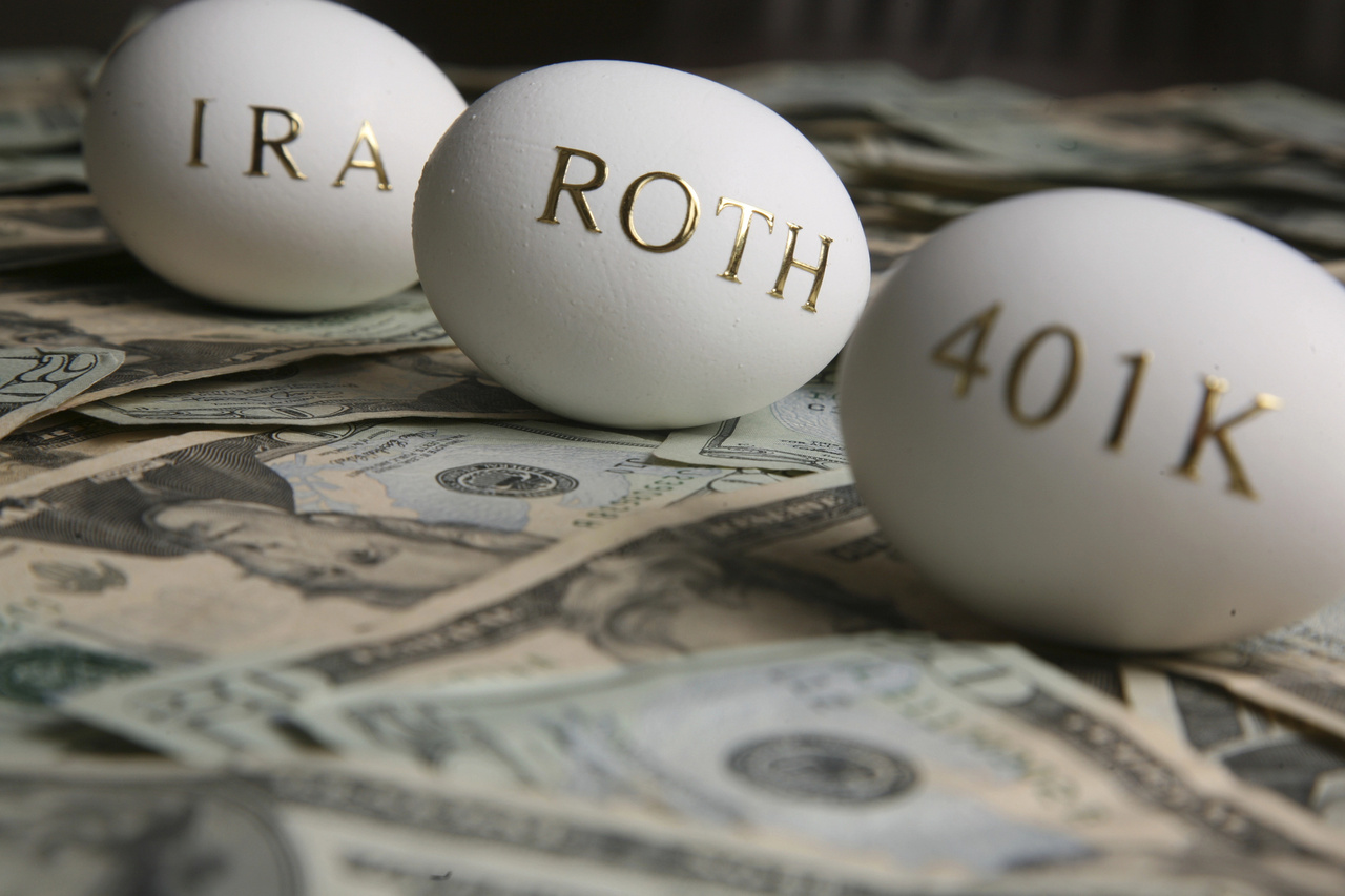 Three eggs labeled IRA, Roth, and 401K resting on a pile of US dollar bills