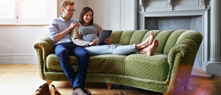 Couple relaxing on a vintage green sofa, looking at a tablet together at home