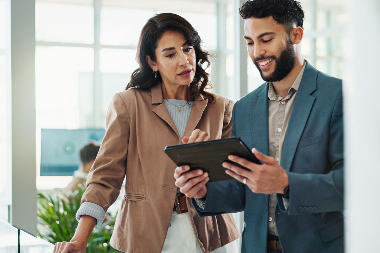 Two business colleagues — a woman and a man — reviewing content on a tablet in an office