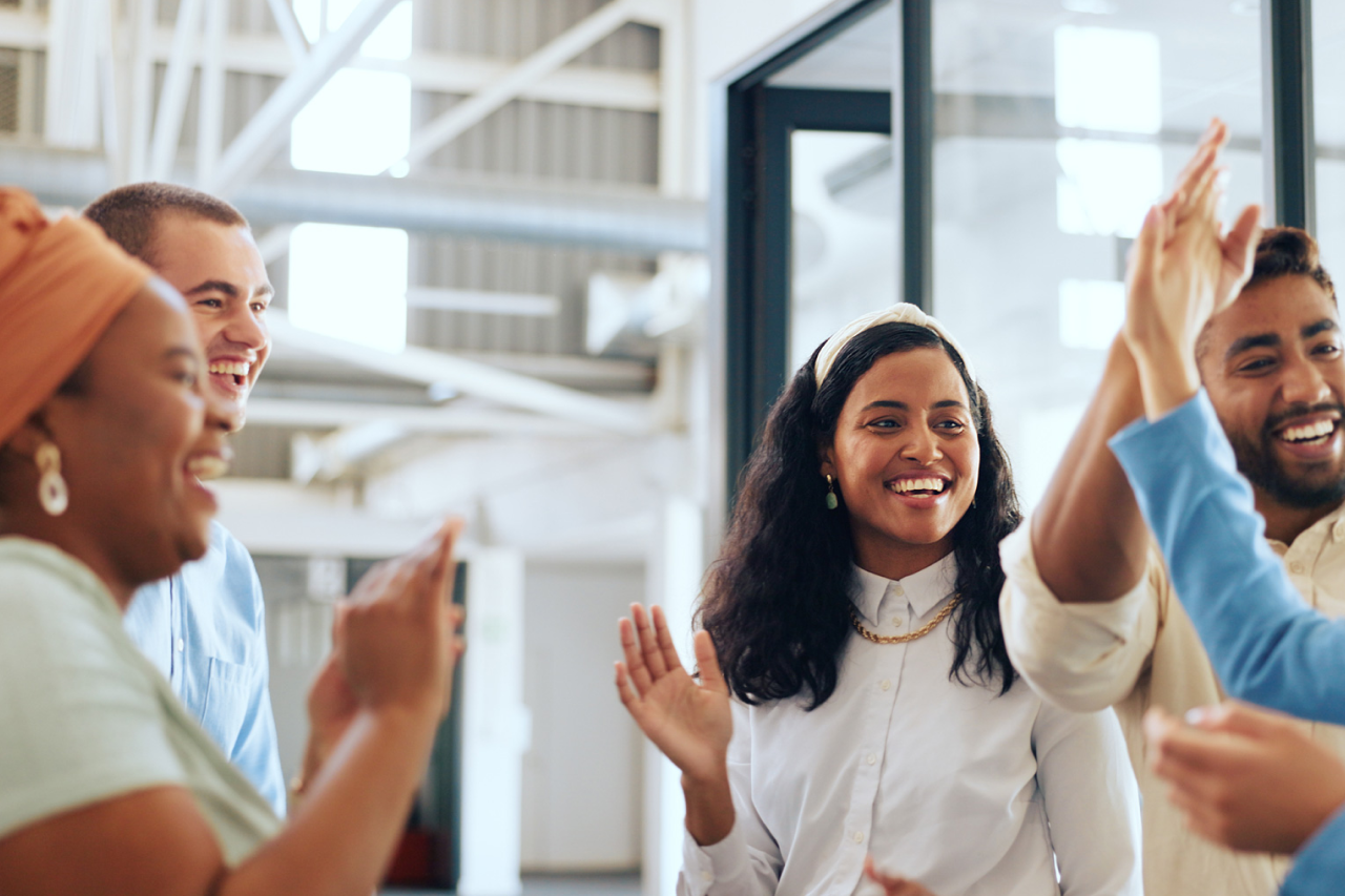 Diverse group of coworkers laughing and giving high fives in a bright, open workspace