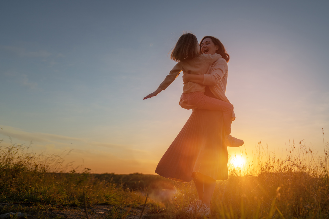 Mother joyfully spinning her young daughter in an embrace against a glowing sunset field